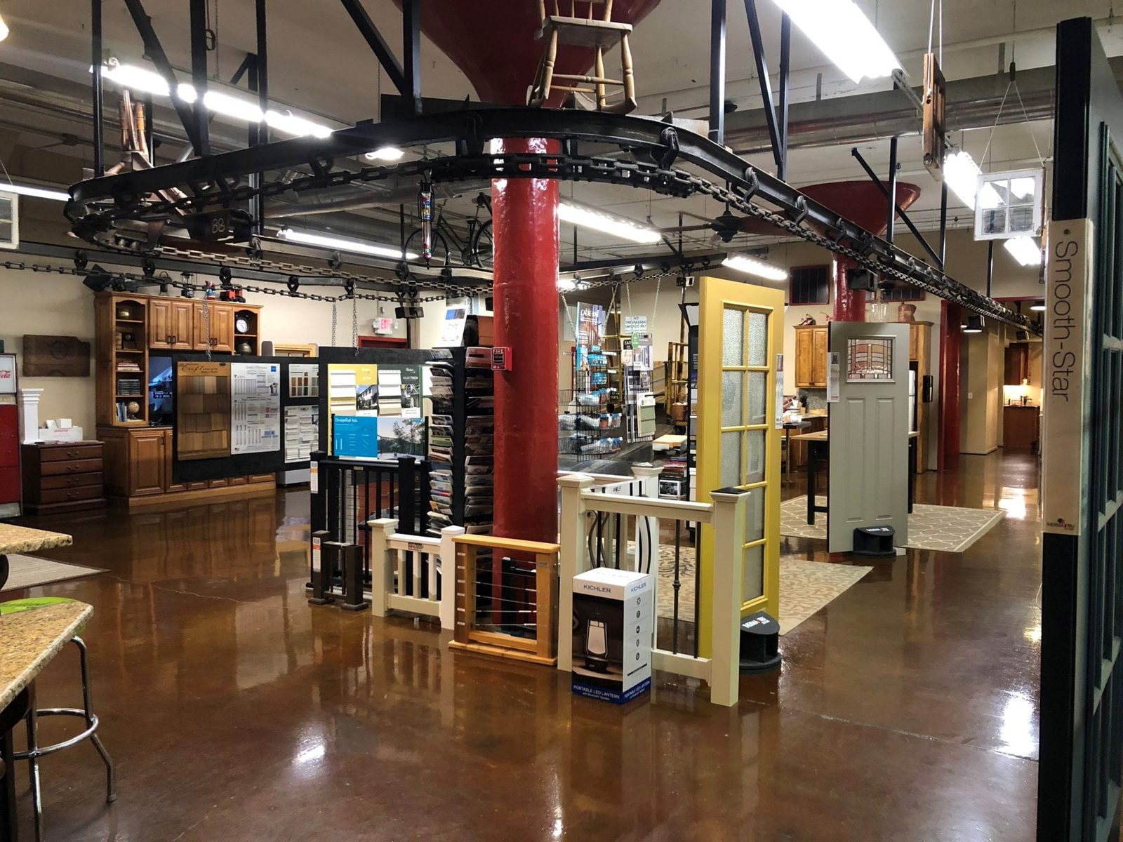Inside the Plyler Supply showroom with door, railing, siding, and column displays under the historic conveyor track